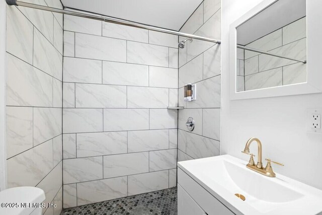 bathroom featuring vanity, a tile shower, and toilet
