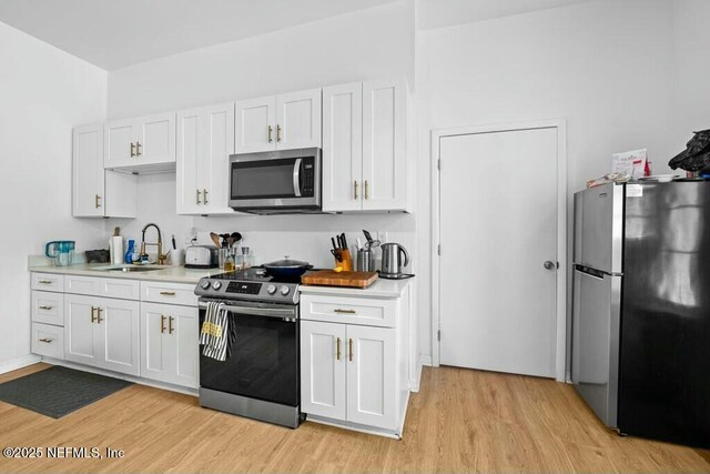kitchen with stainless steel appliances, light wood-type flooring, light countertops, and a sink