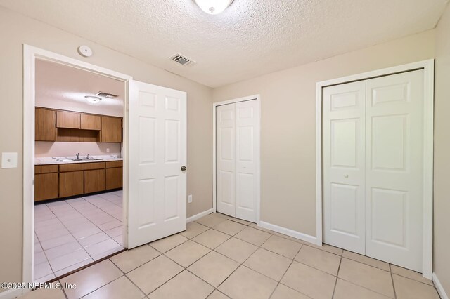 11764 Raven Dr W, Jacksonville, FL 32218 - unfurnished bedroom with visible vents, baseboards, light tile patterned floors, a textured ceiling, and multiple closets