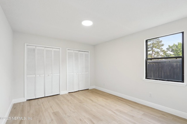 unfurnished bedroom featuring multiple closets, baseboards, and light wood-style flooring