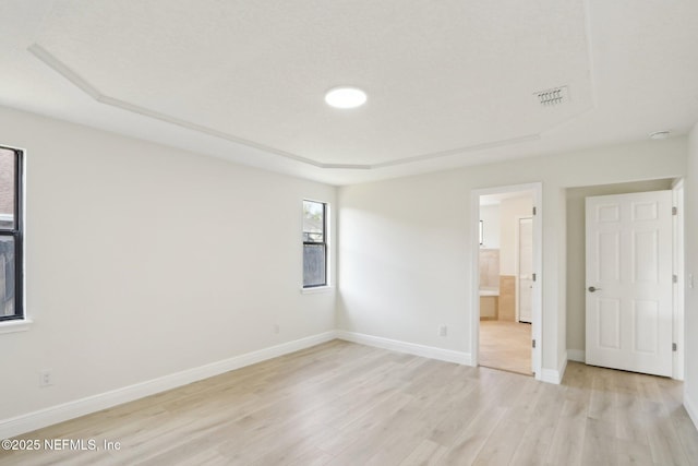 unfurnished bedroom with visible vents, a raised ceiling, baseboards, light wood finished floors, and ensuite bathroom