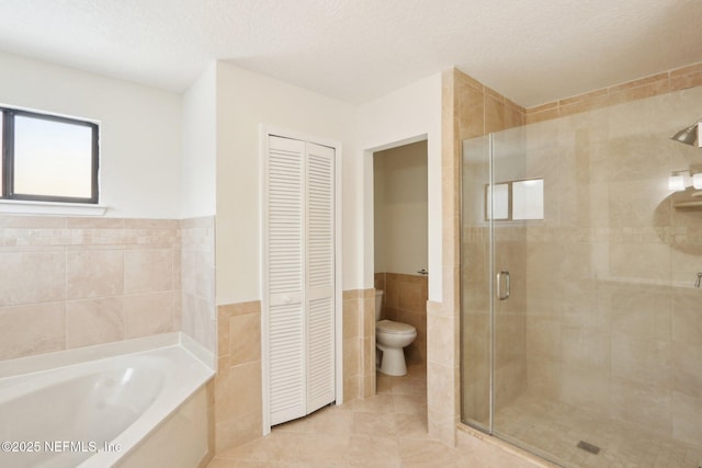 bathroom featuring wainscoting, tile walls, a shower stall, a garden tub, and a closet