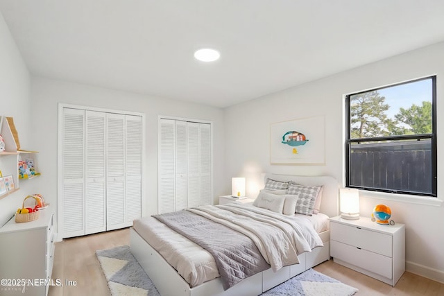 bedroom with baseboards, multiple closets, and light wood-style flooring