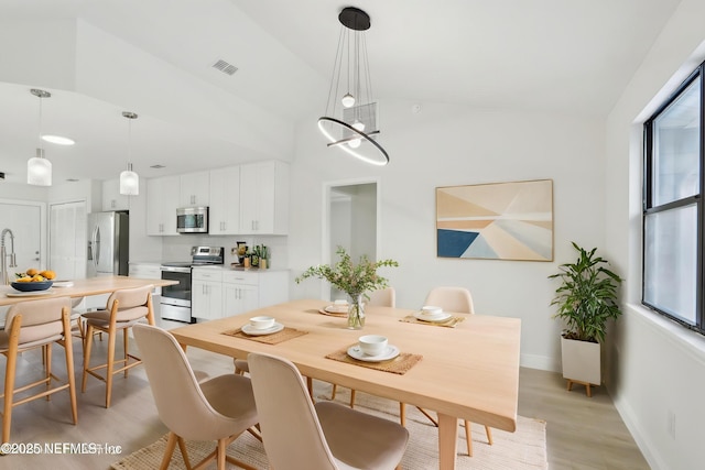 dining area with baseboards, visible vents, vaulted ceiling, and light wood-style floors