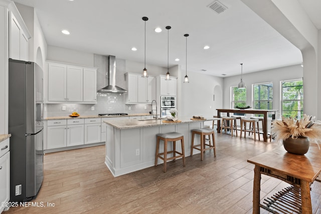 kitchen featuring visible vents, appliances with stainless steel finishes, light wood-type flooring, a sink, and wall chimney exhaust hood
