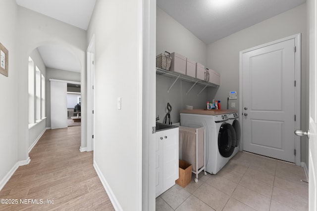 washroom with washing machine and clothes dryer, laundry area, light wood finished floors, arched walkways, and baseboards