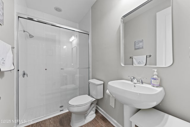 bathroom featuring baseboards, wood finished floors, toilet, and a shower stall