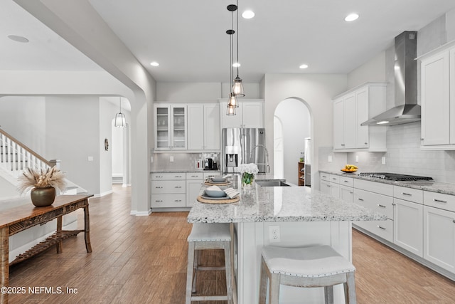 kitchen with wall chimney range hood, arched walkways, tasteful backsplash, a sink, and stainless steel appliances