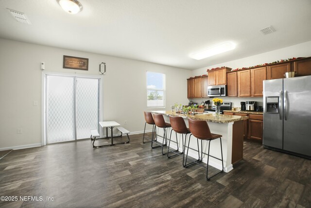 kitchen with a breakfast bar, an island with sink, dark wood-type flooring, visible vents, and stainless steel appliances