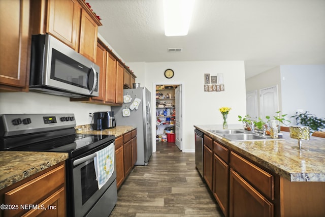 kitchen featuring dark wood-type flooring, visible vents, appliances with stainless steel finishes, a sink, and a center island with sink