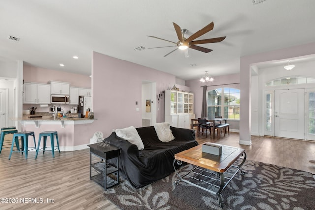 11975 Smith Pointe Ct, Jacksonville, FL 32218 - living room featuring light wood-style flooring, ceiling fan with notable chandelier, baseboards, and visible vents