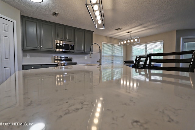 3038 Majestic Oaks Ln, Green Cove Springs, FL 32043 - kitchen featuring a textured ceiling, visible vents, a sink, hanging light fixtures, and stainless steel appliances