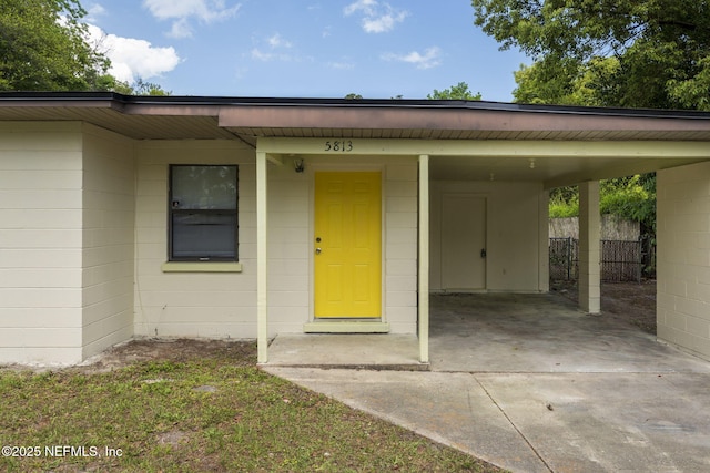 property entrance featuring a carport, fence, concrete block siding, and concrete driveway