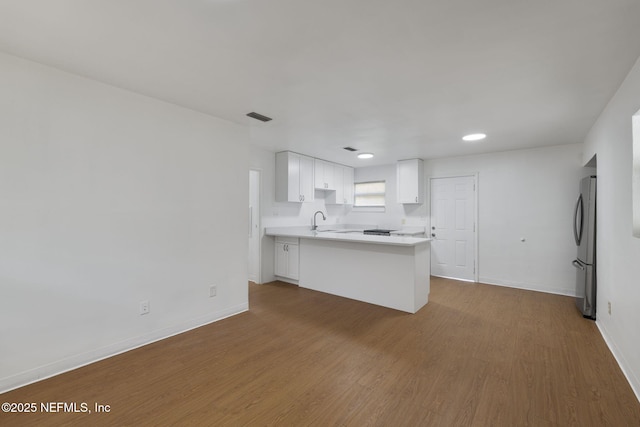 kitchen featuring light countertops, a peninsula, dark wood-type flooring, visible vents, and freestanding refrigerator