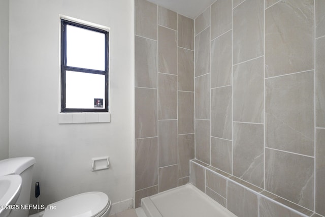 bathroom with baseboards, toilet, and a stall shower
