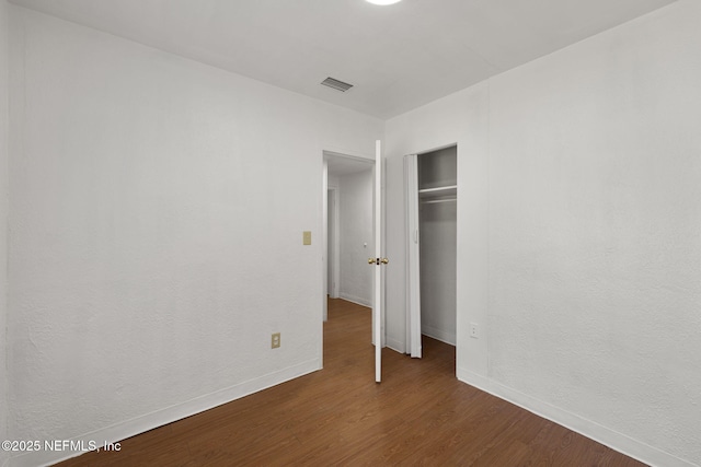 unfurnished bedroom with baseboards, visible vents, dark wood-type flooring, and a closet