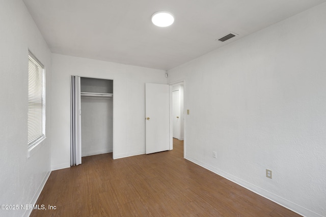 unfurnished bedroom featuring baseboards, wood finished floors, visible vents, and a closet