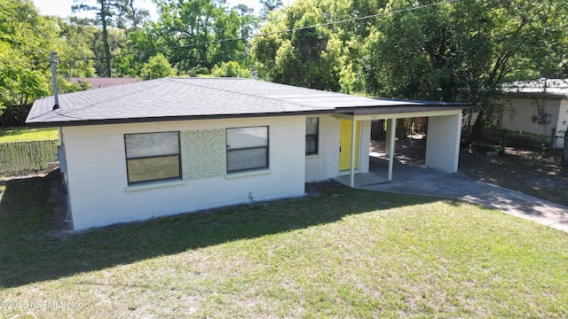 back of property featuring driveway, concrete block siding, a carport, a lawn, and roof with shingles