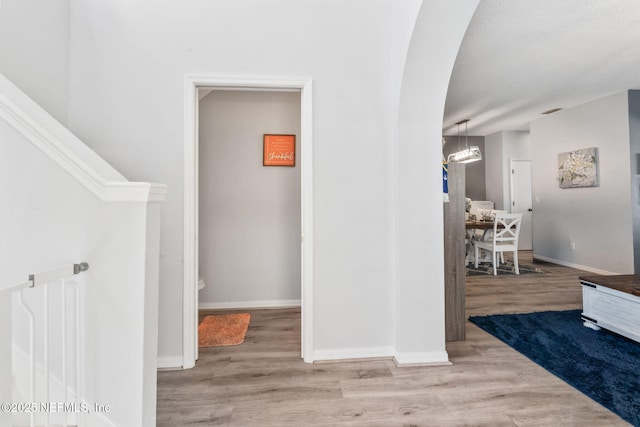 stairs with baseboards, wood finished floors, arched walkways, and a notable chandelier