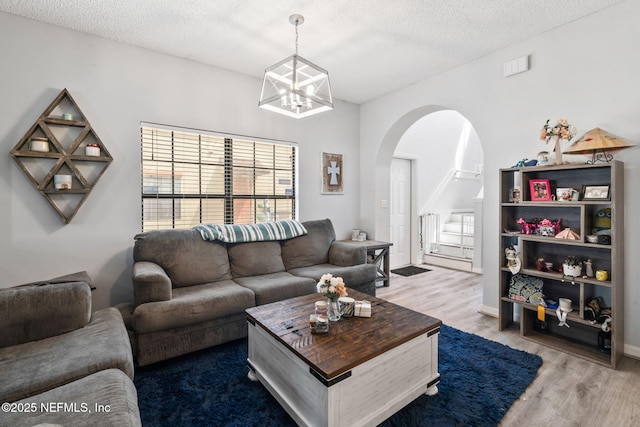 living room featuring wood finished floors, a textured ceiling, stairs, a chandelier, and arched walkways
