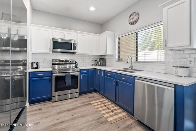 kitchen with white cabinets, blue cabinetry, light countertops, a sink, and appliances with stainless steel finishes