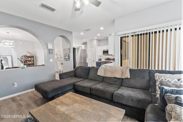 living area with visible vents, wood finished floors, arched walkways, and ceiling fan
