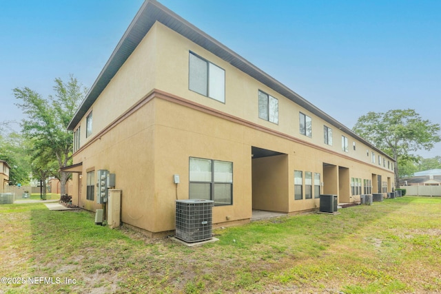 back of property with stucco siding, central AC unit, and a lawn