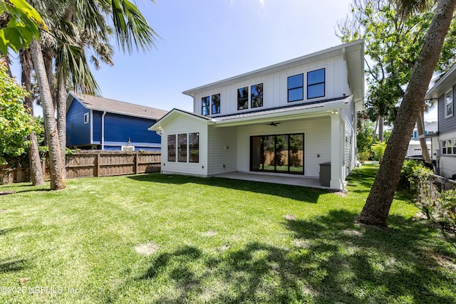 rear view of house featuring a patio, board and batten siding, a ceiling fan, fence, and a lawn