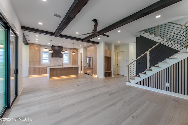 unfurnished living room featuring light wood-style floors, beamed ceiling, ceiling fan, visible vents, and stairway