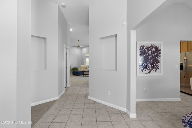 corridor featuring a towering ceiling, baseboards, and light tile patterned flooring