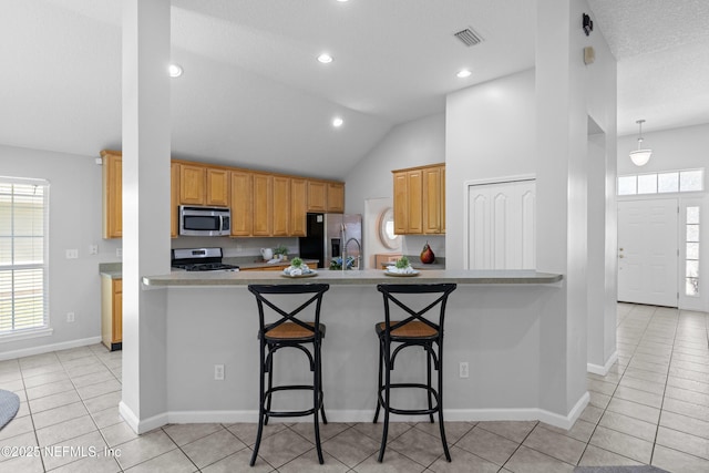 kitchen with a kitchen breakfast bar, stainless steel appliances, light countertops, visible vents, and light tile patterned floors