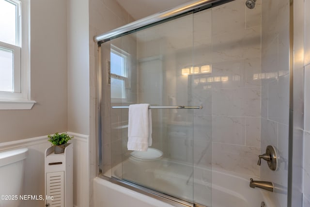 full bathroom with a decorative wall, toilet, bath / shower combo with glass door, and a wainscoted wall