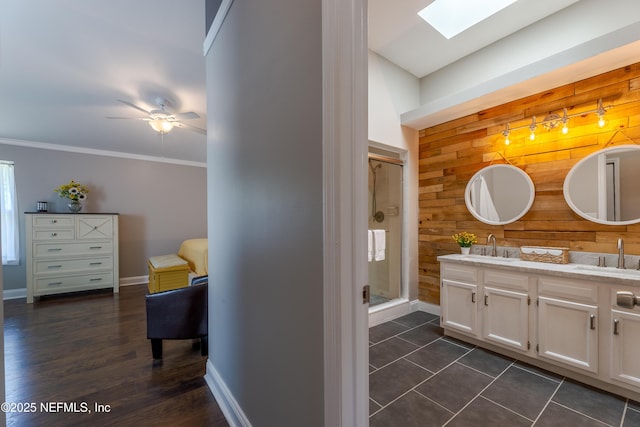 full bath with a sink, baseboards, a skylight, a shower stall, and wooden walls