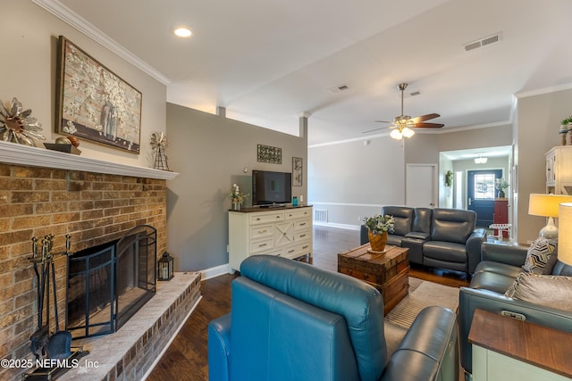 living area with wood finished floors, visible vents, ornamental molding, a brick fireplace, and ceiling fan
