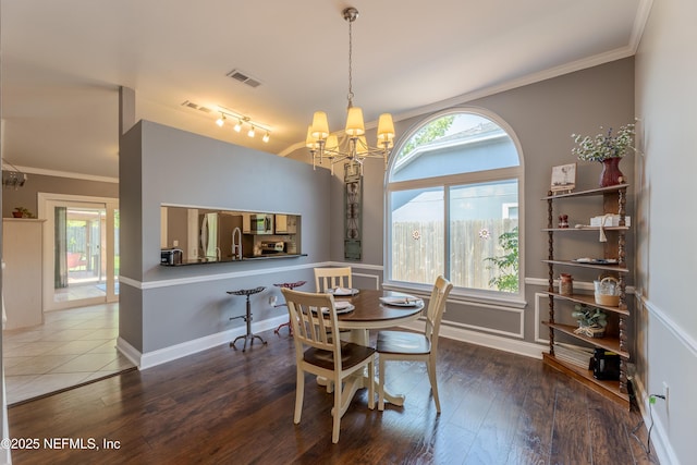 dining area featuring wood-type flooring, visible vents, ornamental molding, and an inviting chandelier