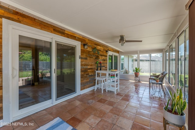 sunroom with a ceiling fan, wood walls, and stone finish flooring