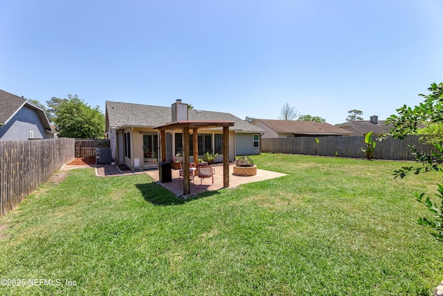 back of house featuring a chimney, a fenced backyard, a yard, a patio area, and a fire pit