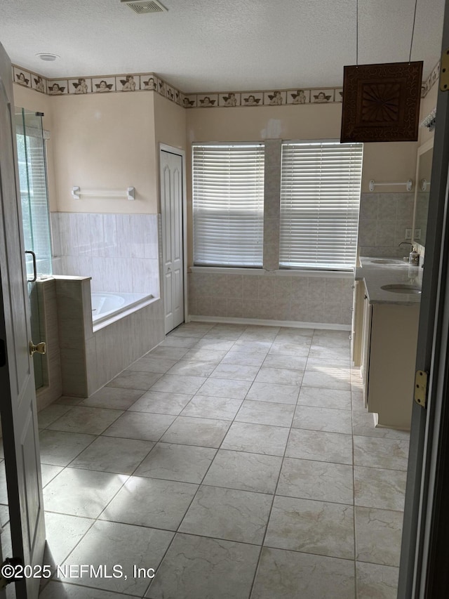 full bathroom featuring a healthy amount of sunlight, vanity, a garden tub, and a textured ceiling
