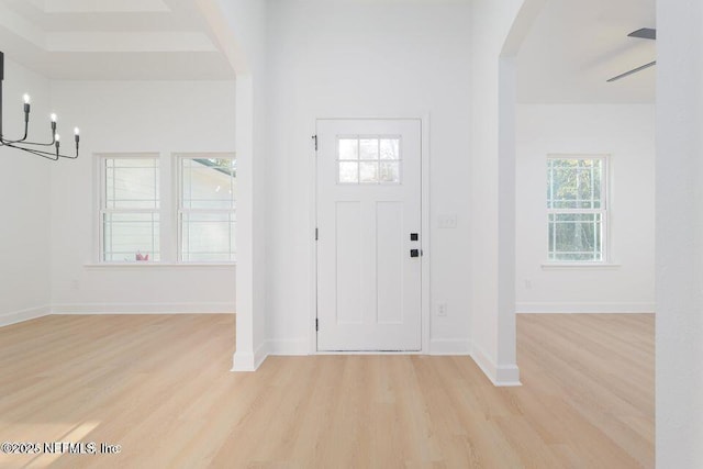 foyer entrance with baseboards, light wood finished floors, arched walkways, and a notable chandelier
