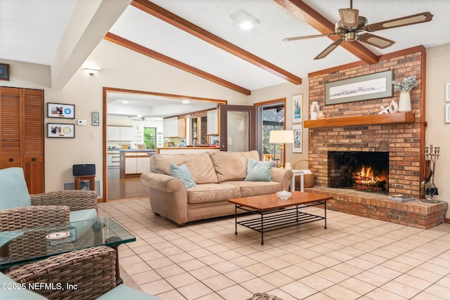 living area with a brick fireplace, a ceiling fan, a textured ceiling, vaulted ceiling with beams, and light tile patterned flooring