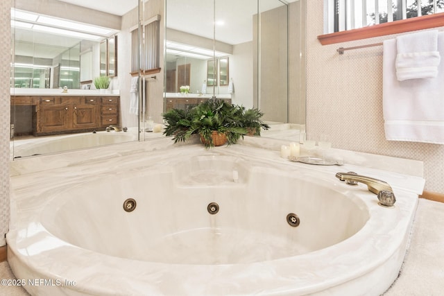 bathroom featuring a jetted tub, vanity, and wallpapered walls