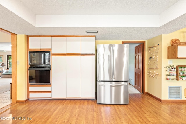 kitchen featuring white cabinets, light wood finished floors, visible vents, and black appliances