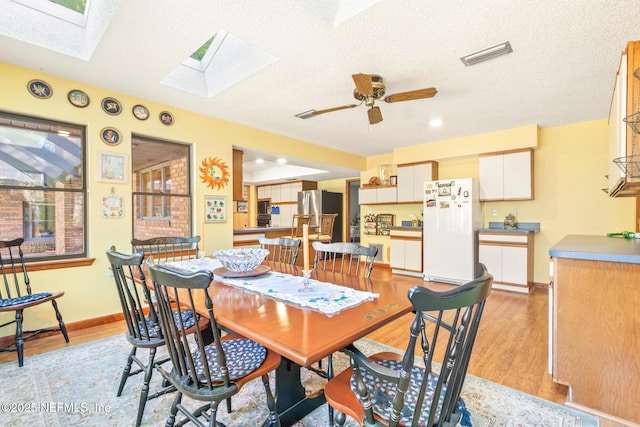 dining area with visible vents, baseboards, a ceiling fan, light wood-style floors, and a skylight