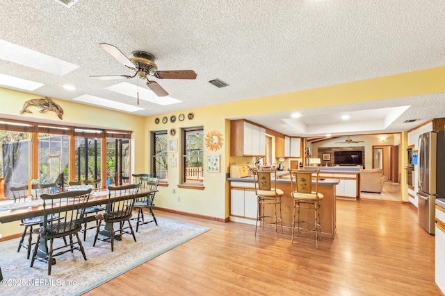 dining room featuring visible vents, baseboards, ceiling fan, light wood-style floors, and a skylight