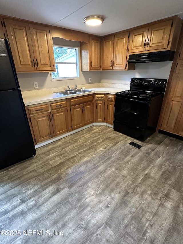 kitchen featuring visible vents, black appliances, under cabinet range hood, a sink, and brown cabinets