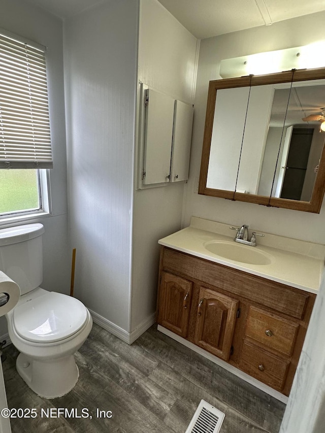 half bath featuring vanity, baseboards, toilet, visible vents, and wood finished floors