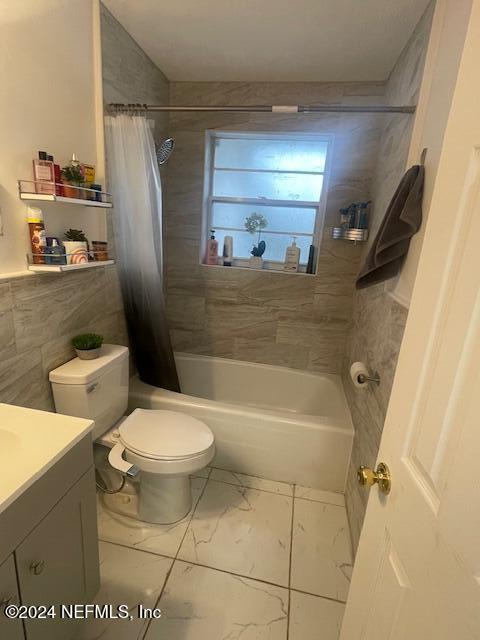 4123 Piper Dr, Jacksonville, FL 32207 - full bathroom featuring shower / bath combination with curtain, vanity, toilet, marble finish floor, and tile walls