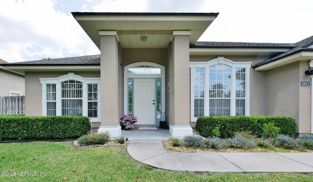 2612 S Waterleaf Dr, Saint Augustine, FL 32092 - view of exterior entry featuring stucco siding, roof with shingles, and a yard