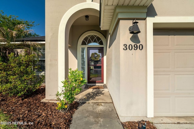 view of exterior entry with a garage and stucco siding
