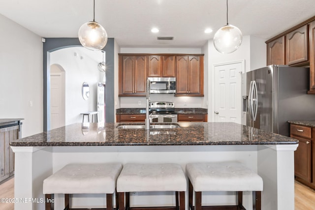 kitchen featuring arched walkways, a breakfast bar, a center island with sink, light wood-style flooring, and stainless steel appliances